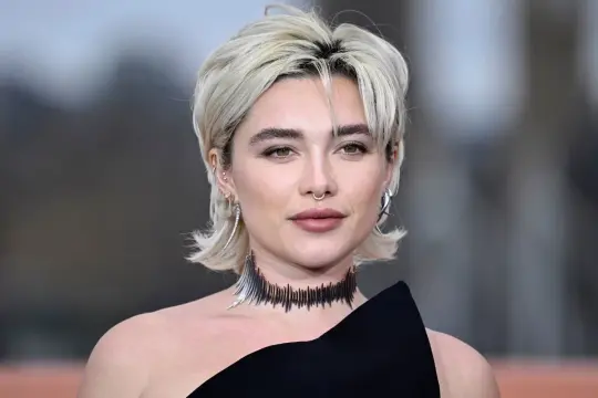 Krótkie, blond włosy z grzywką, kolczyki i naszyjnik nawiązują do modnych fryzur lat 80.