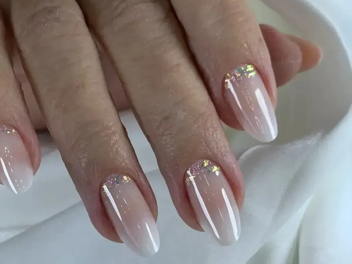 Eleganckie paznokcie w stylu babyboomer z subtelnym brokatem. Delikatny gradient od cielistego różu do bieli, ozdobiony iskrzącymi drobinkami.