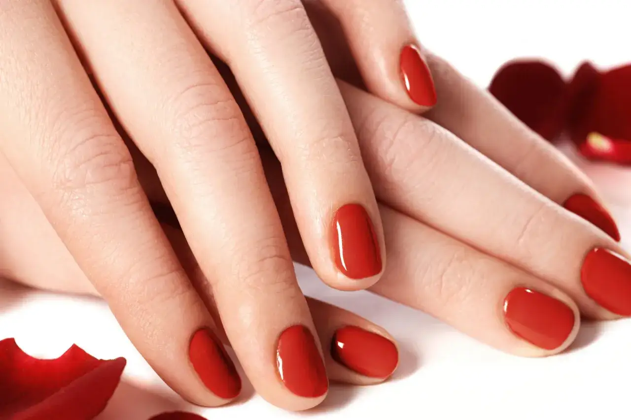 Dłonie z idealnym, czerwonym manicure. Te tytanowe paznokcie lśnią niczym drogocenne kamienie, otoczone płatkami czerwonych róż.